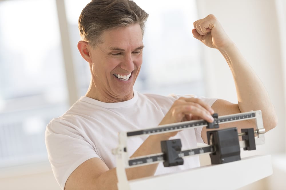Man celebrating weight loss progress after GLP-1 treatment while checking results on a scale