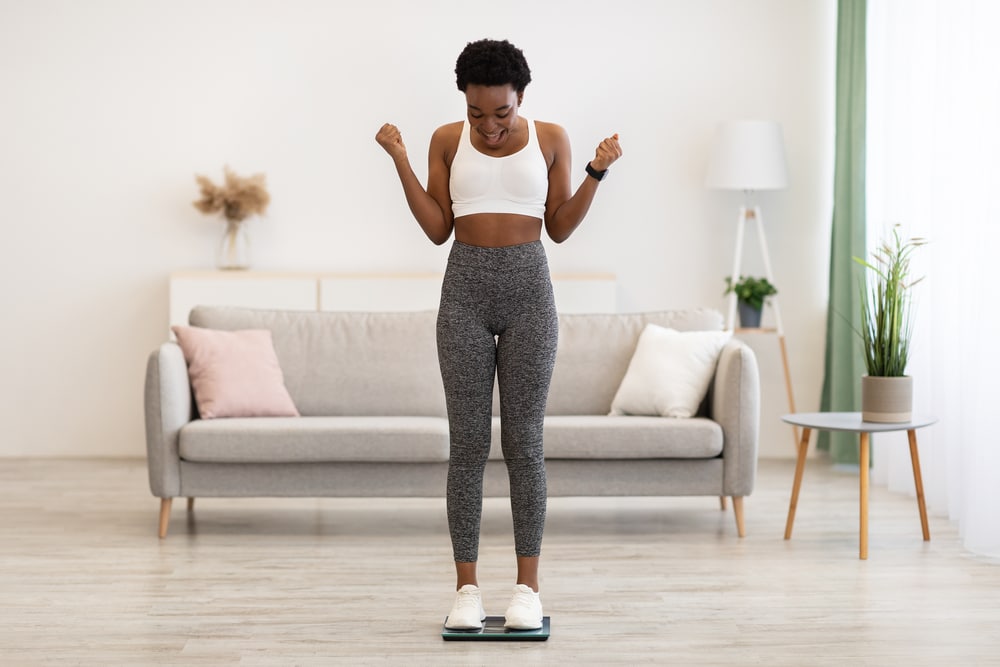 Woman smiling on a scale during GLP-1 weight loss progress.